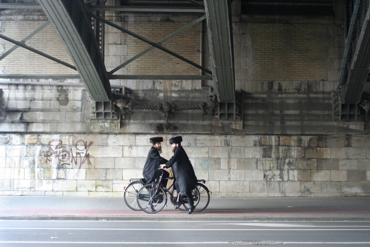 Two men on bicycles meeting under a bridge