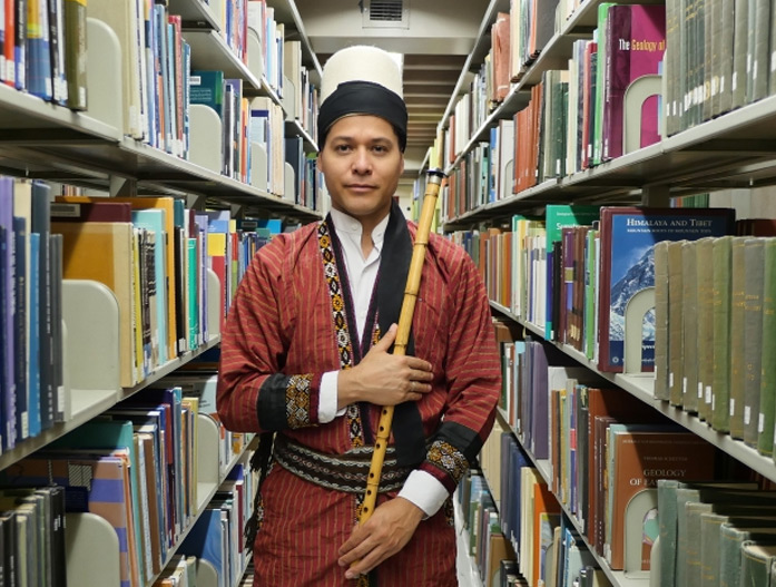 Juan Castrillón holding a ney in library stacks