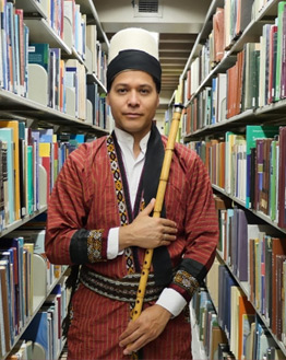Juan Castrillón holding a ney in library stacks