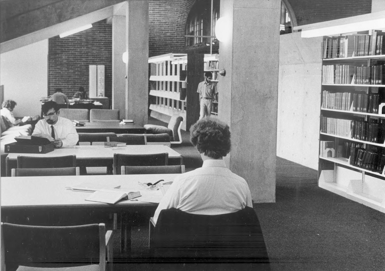 Stacks, 2 students in neckties sitting at tables. The structure comprises concrete columns supporting a sloped concrete slab.