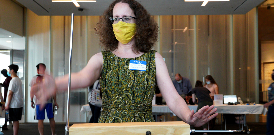 A woman wearing a face mask stands with her hands stretched out in front of her, playing the theremin  