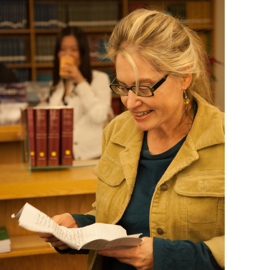 Blonde woman stands in a library smiling down at a document