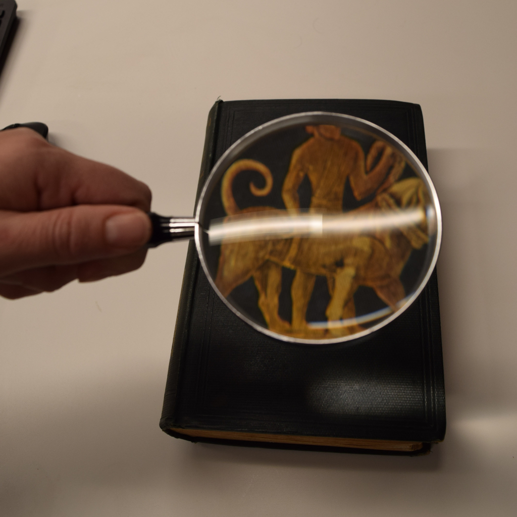 Magnifying glass enhances book cover showing image of a figure riding a large animal