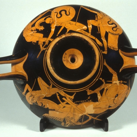 A ceramic cup with a black background and an illustration of ancient Greek soldiers falling to the ground.