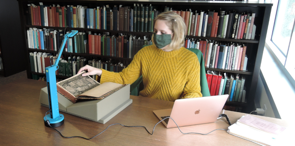 A person wearing a face mask turns the page in a manuscript while streaming on a laptop.