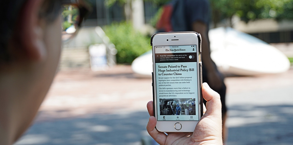 Individual holding mobile phone on Penn's campus with NYTimes app visible on screen