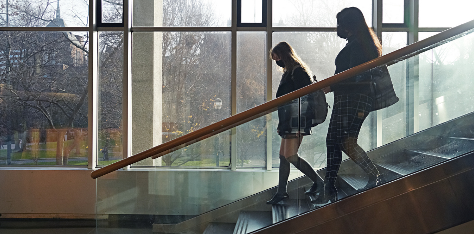 Two students, shown in silhouette, walk down Van Pelt Library's stairs in front of an open window