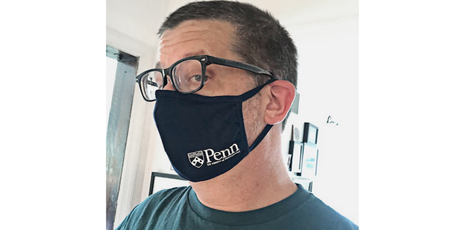A man wearing a face mask with the University of Pennsylvania logo on it.