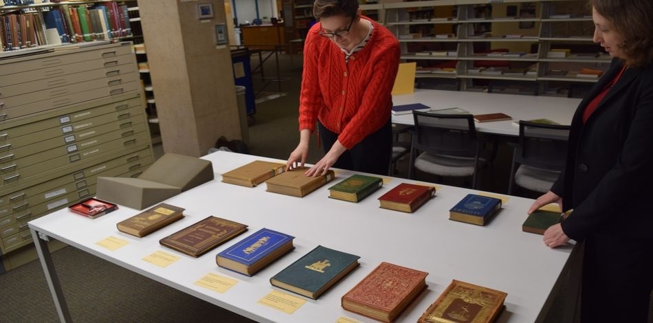 Two people review a display of rare books on a table