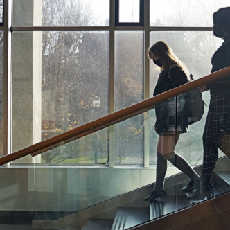 Two students, shown in silhouette, walk down Van Pelt Library's stairs in front of an open window
