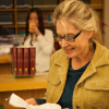 A woman stands in a library, smiling down at a document.
