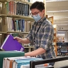 A masked individual moves books from a shelf to a rolling cart