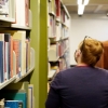 A person with red hair walks away from a camera next to a book shelf